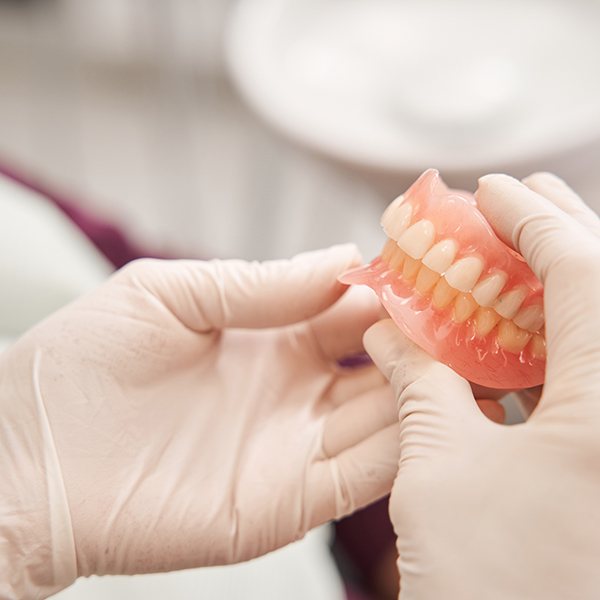 Hands in white gloves holding a full set of dentures